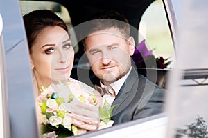 Portrait of a young loving couple newlyweds next to a bouquet in the window of a wedding car.