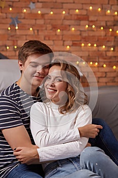 Portrait of a young loving couple resting on a grey couch together at home and hugging