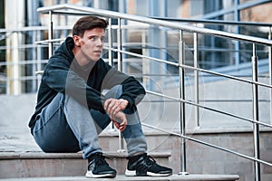 Portrait of young main in black clothes that sits on the stairs and taking a break