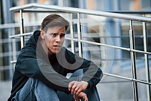 Portrait of young main in black clothes that sits on the stairs and taking a break