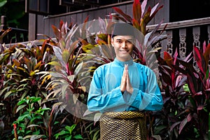 A portrait of young malay man in his traditional teal cloth, samping songket and songkok. Selamat Hari Raya gesture photo