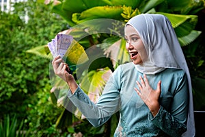 A portrait of young malay woman with surprise expression, holding an envelope of pocket money or raya angpao of Malaysian Currency