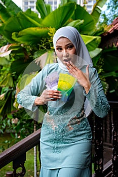 A portrait of young malay woman with surprise expression, holding an envelope of pocket money or raya angpao of Malaysian Currency