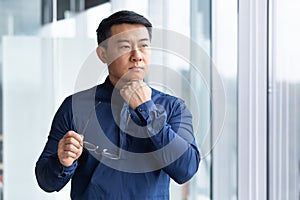 Portrait of a young male Asian teacher. He is standing in the office, looking in the window