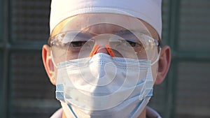 Portrait of young male caucasian doctor with medical face mask looks at camera. Medical worker wearing protective mask
