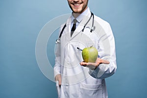 Portrait Of Young Male Doctor Holding Green Apple. Isolated On Light Blue.