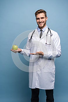 Portrait Of Young Male Doctor Holding Green Apple. Isolated On Light Blue.