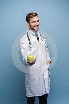Portrait Of Young Male Doctor Holding Green Apple. Isolated On Light Blue.