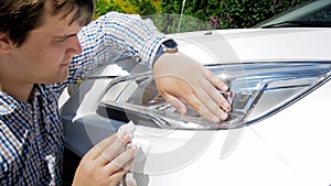 Portrait of young male driver cleaning car headlamps