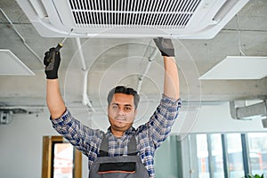 Portrait of young male indian technician repairing air conditioner. Air conditioner repairs.