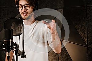 Portrait of young male musician in headphones sensually singing recording song in modern studio