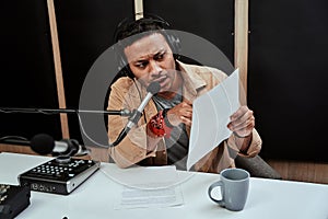 Portrait of young male radio host looking serious while reading a script paper, getting ready for moderating a live show