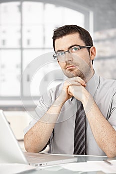 Portrait of young male sitting at desk thinking