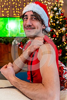 Portrait of a young male smiling after getting a vaccine - Man showing her arm with bandaid during a Christmas party