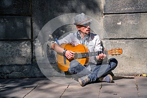 Portrait of young male street musician playing guitar on a city sidewalk. Freedom, music and art concept. Horizontal image