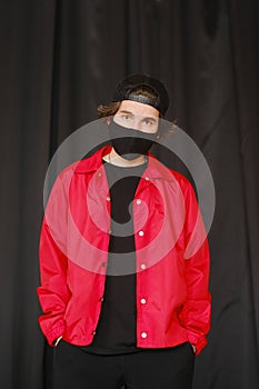 Portrait of a young man 25-30 years old in a black protective mask, black cap and red jacket.