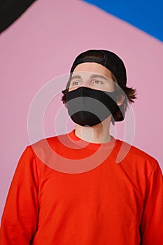 Portrait of a young man 25-30 years old in a black protective mask, black cap and red jacket.