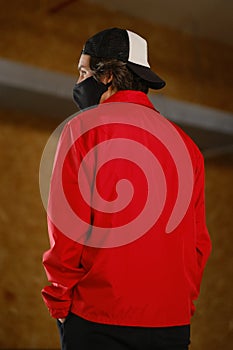 Portrait of a young man 25-30 years old in a black protective mask, black cap and red jacket.