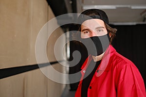 Portrait of a young man 25-30 years old in a black protective mask, black cap and red jacket.