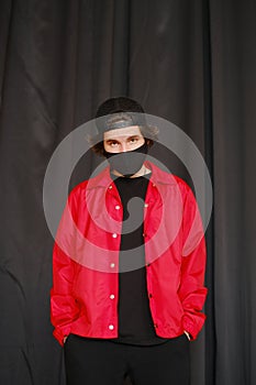 Portrait of a young man 25-30 years old in a black protective mask, black cap and red jacket.