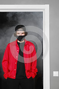 Portrait of a young man of 25-30 years old in a black protective mask, cap and red jacket.