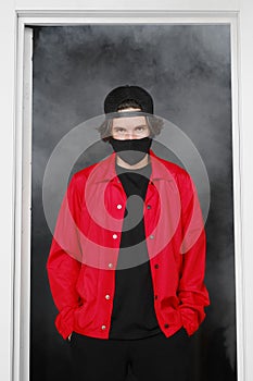 Portrait of a young man of 25-30 years old in a black protective mask, cap and red jacket.