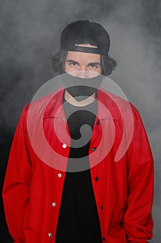 Portrait of a young man of 25-30 years old in a black protective mask, cap and red jacket.