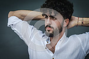 Portrait of a young man with beard and curly hair, who relaxes by stretching his back with his hands behind his neck