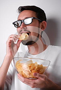 portrait of a young man with a beard wearing 3d glasses eating chips