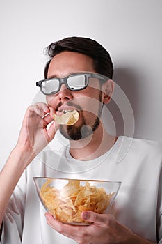 portrait of a young man with a beard wearing 3d glasses eating chips