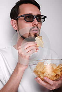 portrait of a young man with a beard wearing 3d glasses eating chips