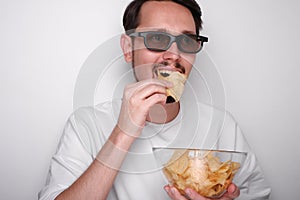 portrait of a young man with a beard wearing 3d glasses eating chips