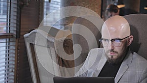 Portrait of young man with beard, wearing a suit in the glasses looking to the monitor laptop. Successful people