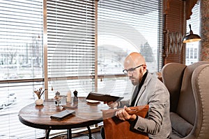 Portrait of young man with beard, wearing a suit in the glasses Puts the laptop in a leather bag. Successful people