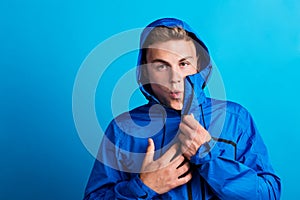 Portrait of a young man with blue anorak in a studio, feeling cold. Copy space.