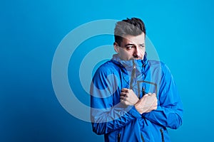 Portrait of a young man with blue anorak in a studio, feeling cold. Copy space. photo