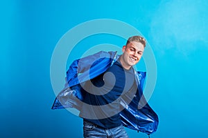 Portrait of a young man with blue anorak in a studio, standing against blue background.