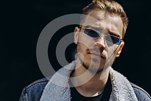 Portrait of young man in blue jeans jacket with sunglasses outdoor on dark background