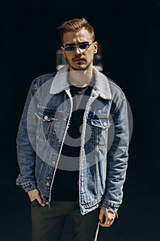 Portrait of young man in blue jeans jacket with sunglasses outdoor on dark background