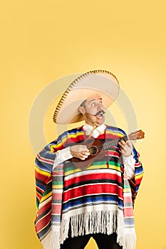 Portrait of young man in bright garment, poncho isolated over yellow background
