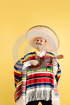 Portrait of young man in bright garment, poncho isolated over yellow background