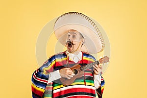 Portrait of young man in bright garment, poncho isolated over yellow background