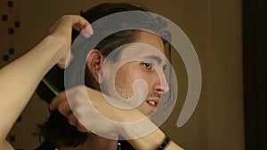 Portrait of young man brushing long layered dark brown hair in bathroom, standing in front of mirror, face profile