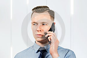 Portrait of young man businessman dressed in blue shirt and tie, talking on the mobile phone