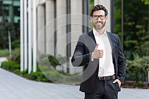 Portrait of a young man businessman, lawyer in a business suit standing outside an office building, smiling at the