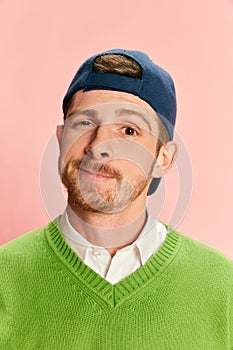 Portrait of young man in cap posing in green sweater and shirt isolated over pink background.