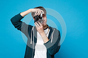 Portrait of young man in casual clothes holding taking pictures on retro vintage photo camera isolated on blue wall