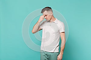 Portrait of young man in casual clothes with lowered head putting hand on nose isolated on blue turquoise wall