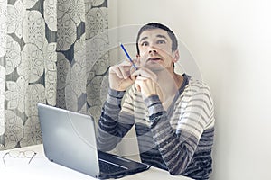 Portrait of young man In casual wear on the job working on laptop, looking at with thoughtful face