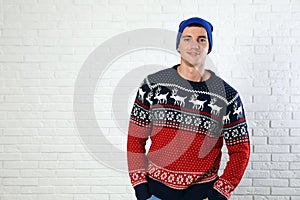 Portrait of young man in Christmas sweater and hat near white brick wall